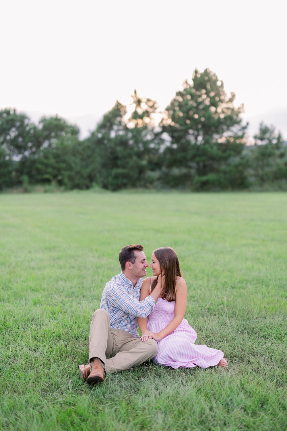 Two people share an intimate moment while sitting in a serene meadow.