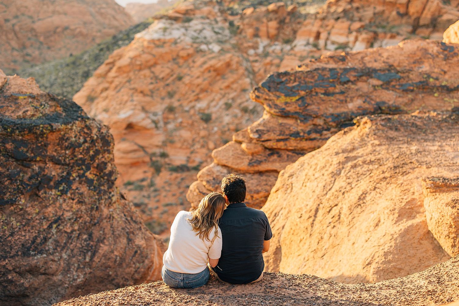 Two people sit at the edge of a scenic canyon overlook during golden hour at Waimea Canyon in Hawaii.