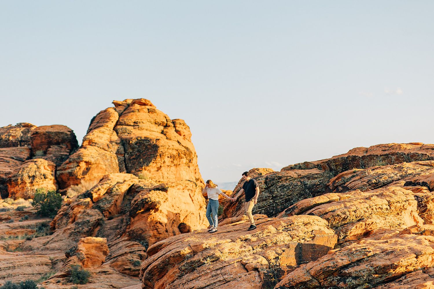 Person in turquoise jacket stands on golden sandstone rock formations during sunset at Arches National Park.