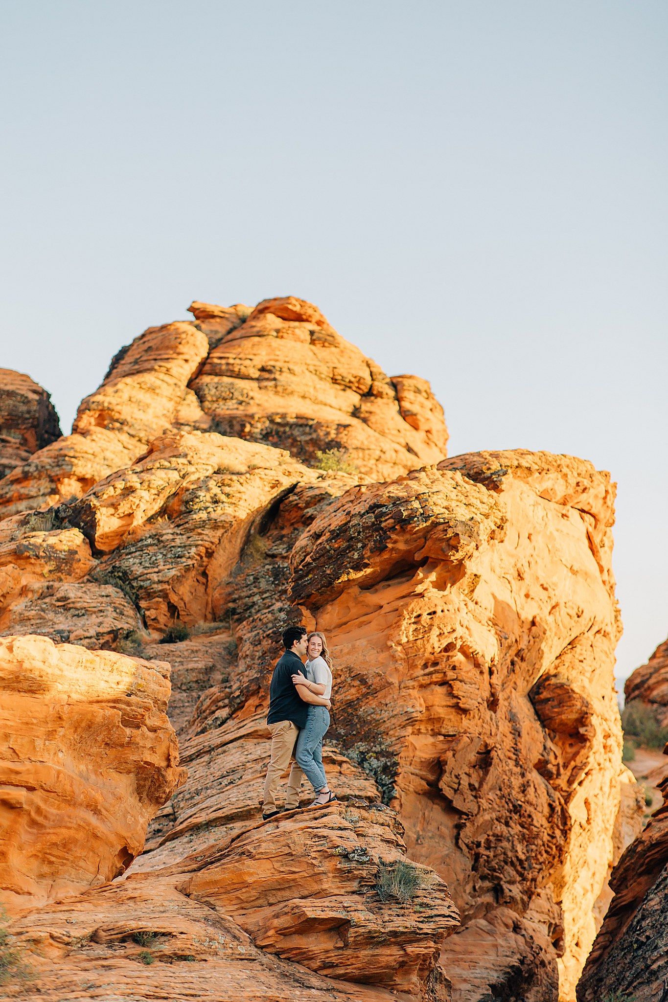 A hiker climbs up steep red sandstone rock formations in a desert landscape during golden hour lighting.