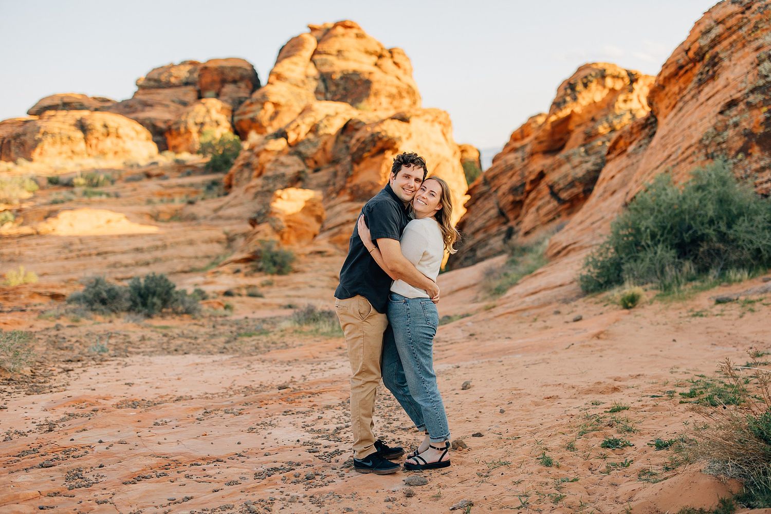 Desert engagement photoshoot with couple posing against red rock formations at golden hour.