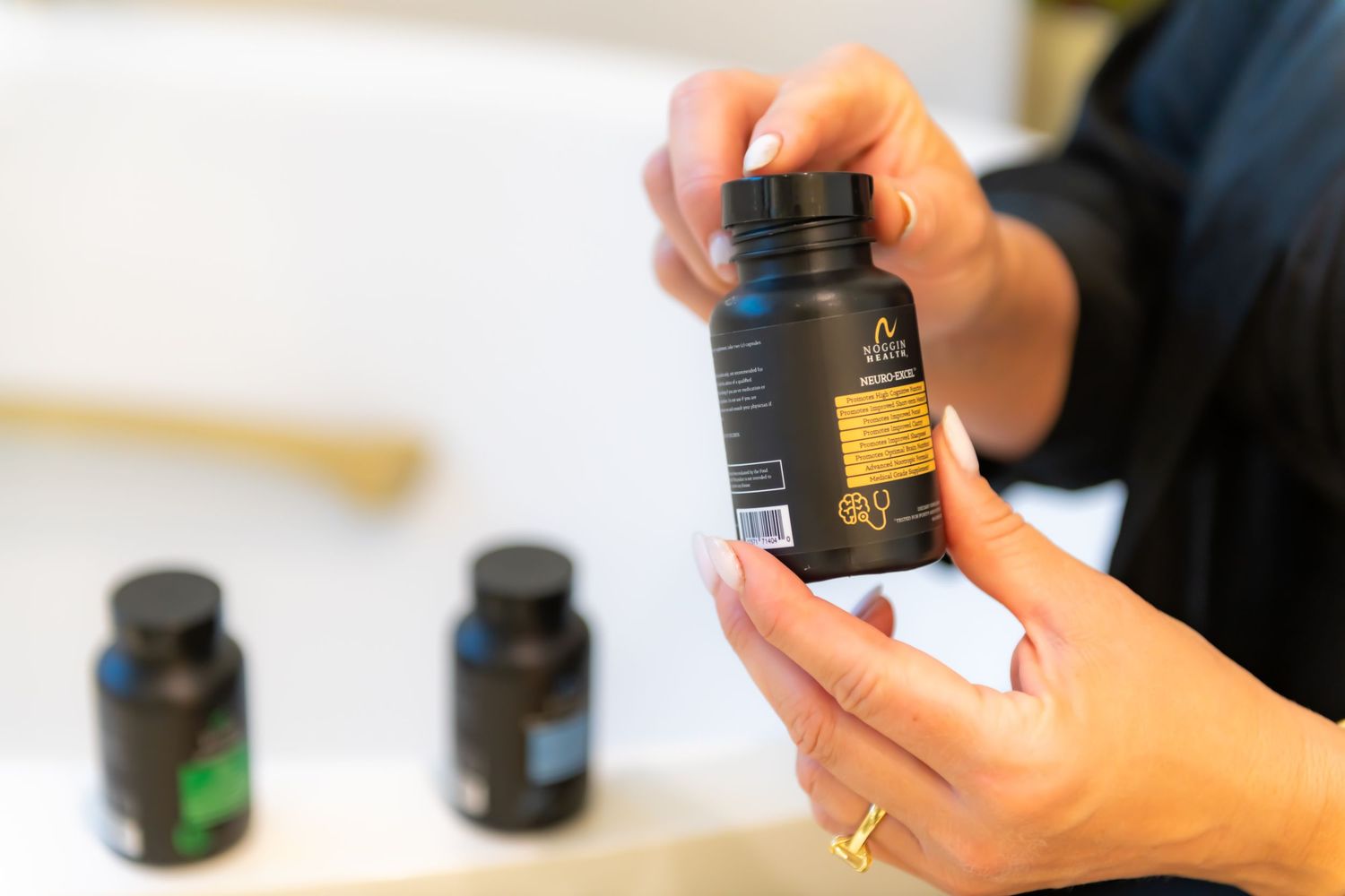 Hands holding and examining dark glass bottles of skincare or wellness products against a white background.