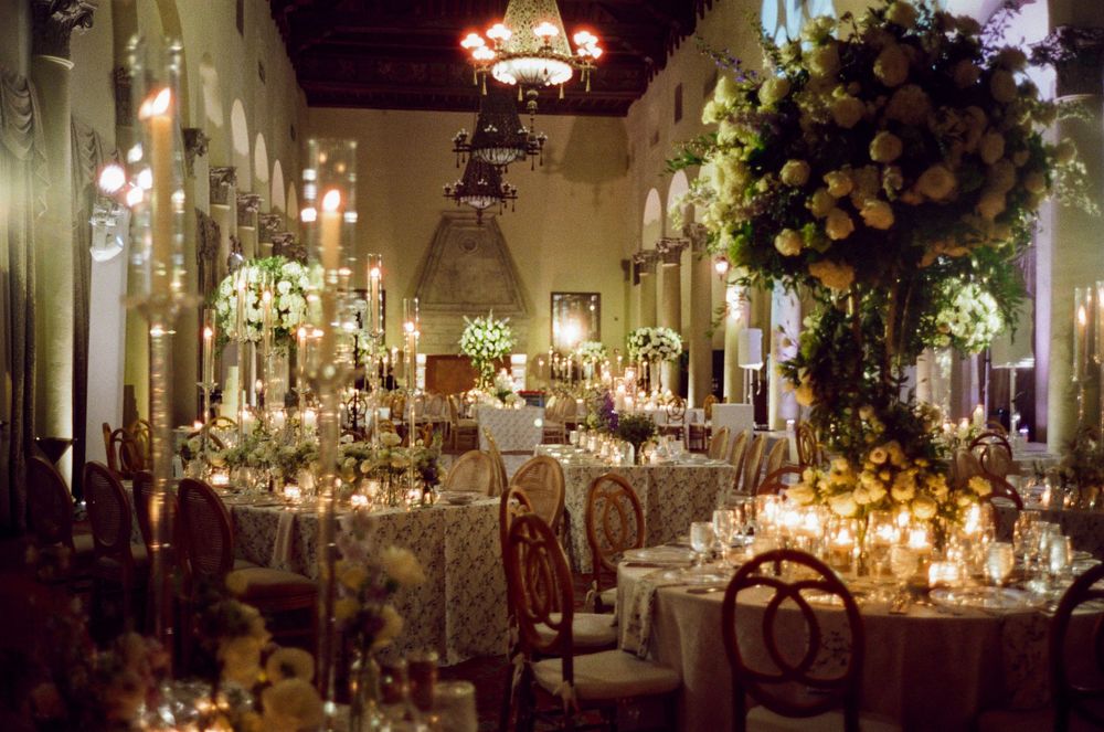 Elegant wedding reception hall decorated with crystal chandeliers, candlelit tables, and floral arrangements in warm lighting.