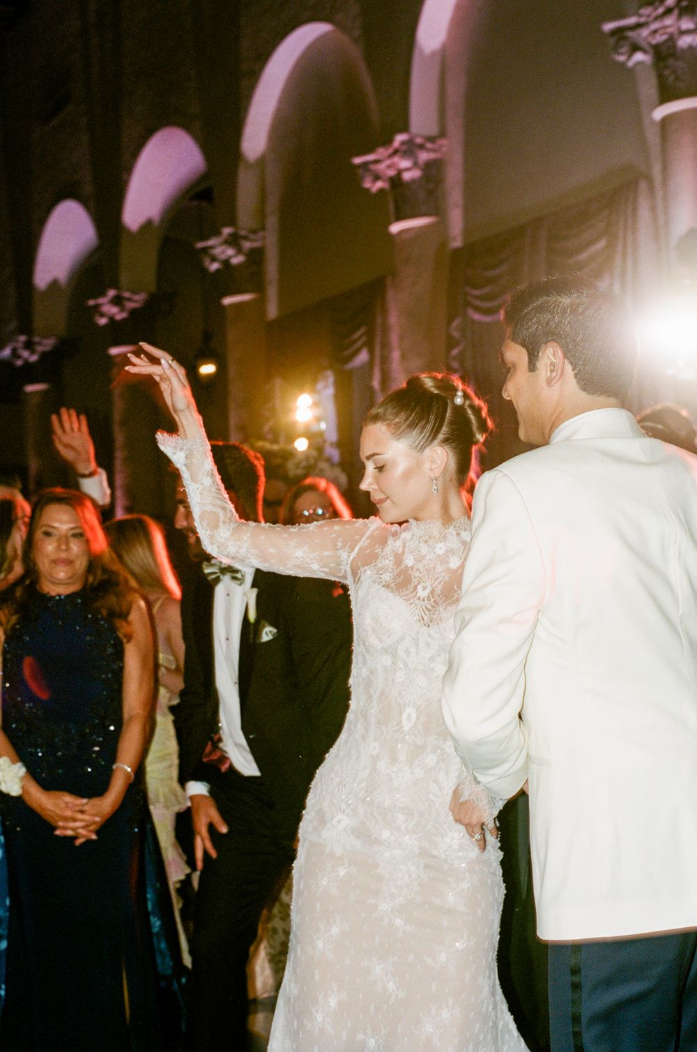 Wedding guests dance and celebrate on the dance floor as the bride in a white sequined gown twirls with joy.