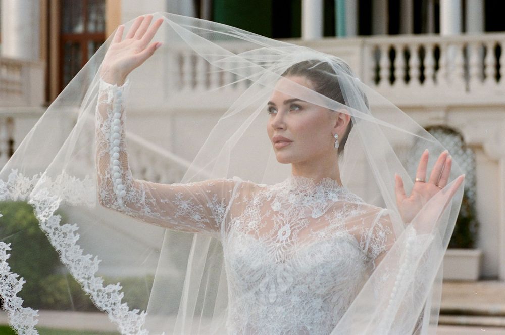 A bride wearing a delicate lace veil and embellished wedding gown poses elegantly in a formal setting.