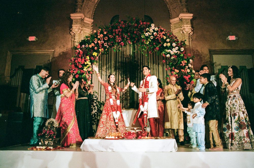Vibrant Indian wedding ceremony with couple under floral arch, surrounded by family in colorful traditional attire.