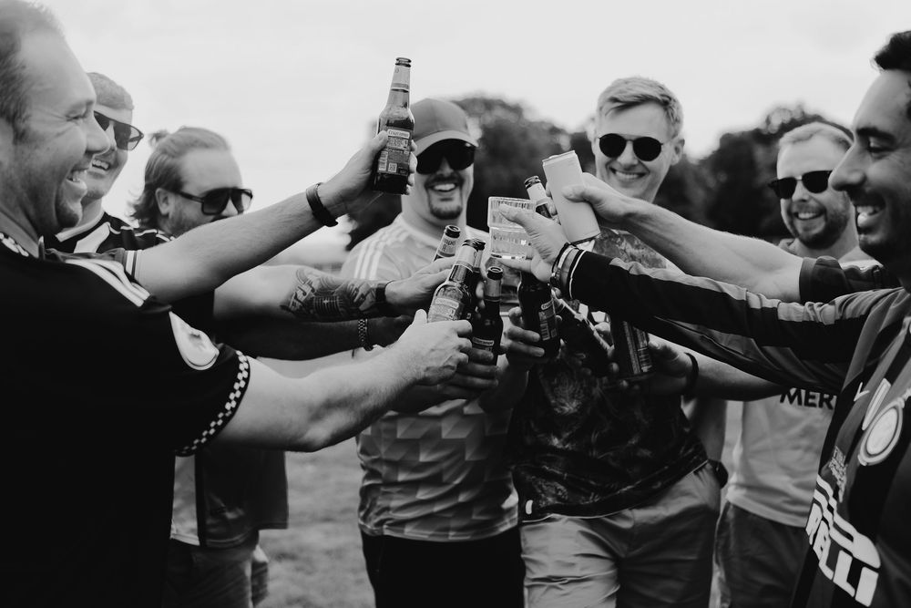 Group of groomsmen toasting with drinks at outdoor wedding celebration.