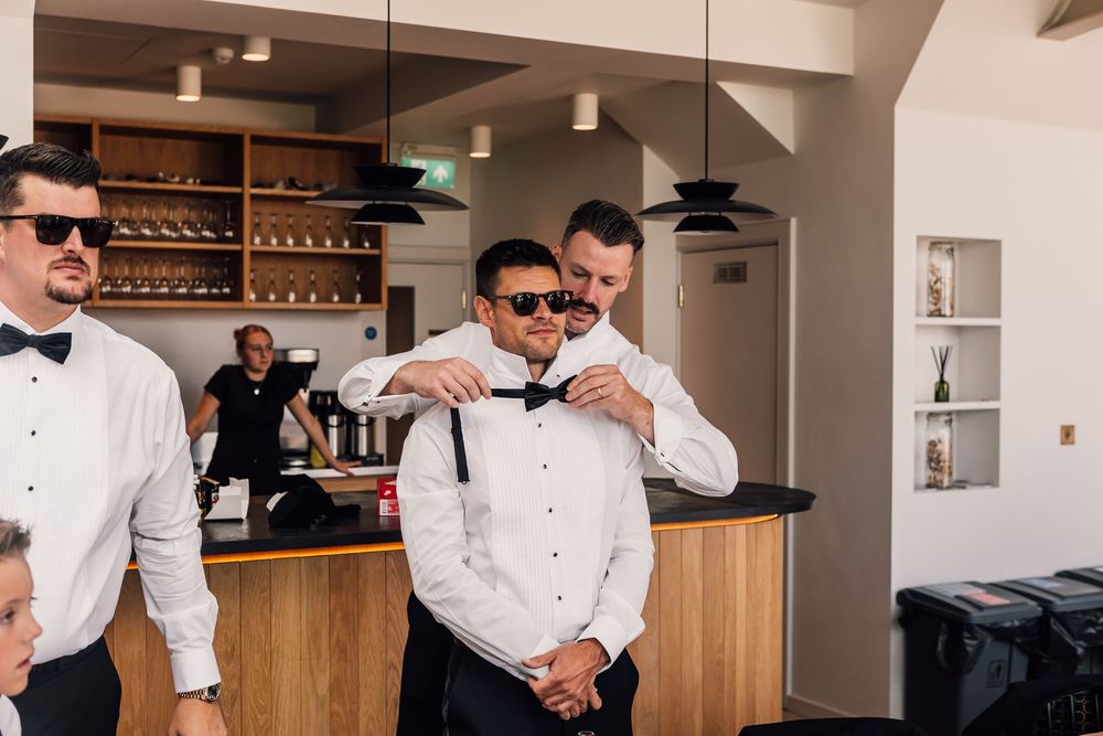 A group of groomsmen in white dress shirts and bow ties prepare for a wedding celebration in a modern venue.