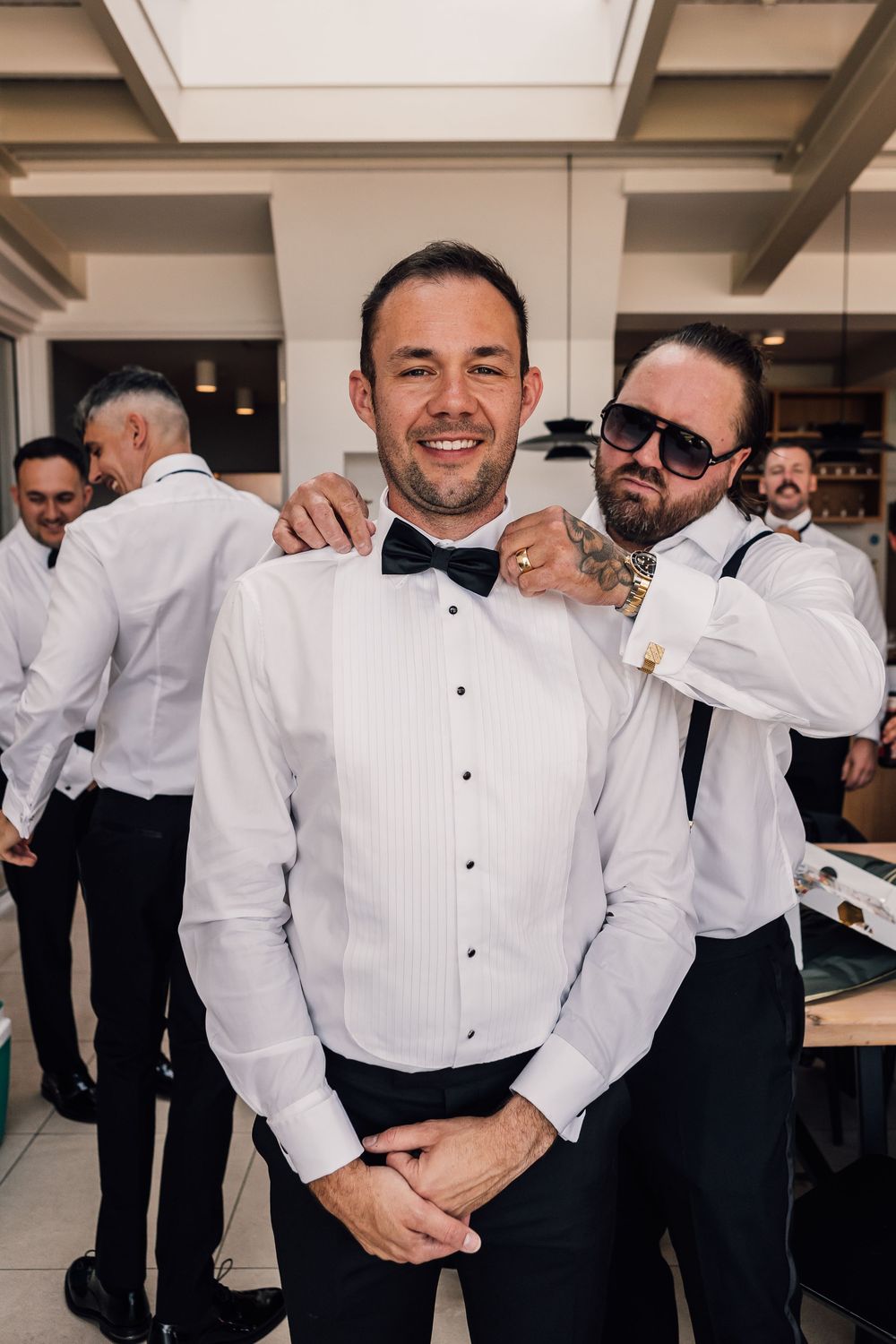 Groomsmen in white tuxedo shirts and black pants getting ready for the wedding celebration.