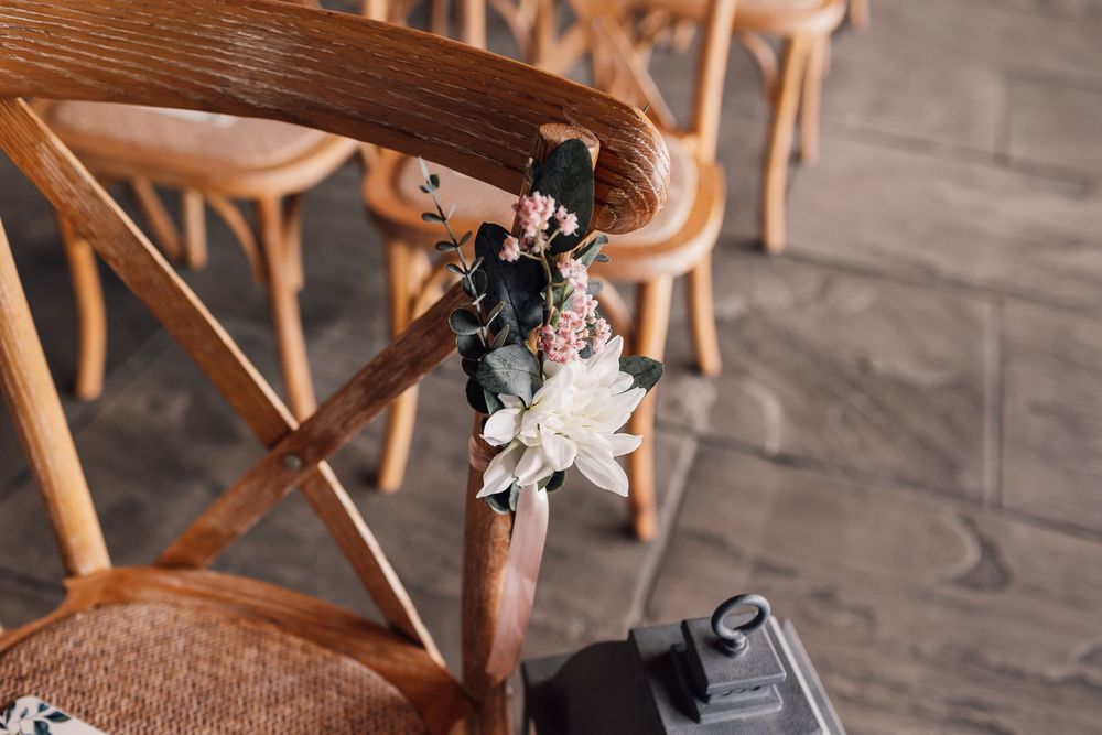 Rustic wooden crossback chairs arranged for wedding ceremony with floral decorations.