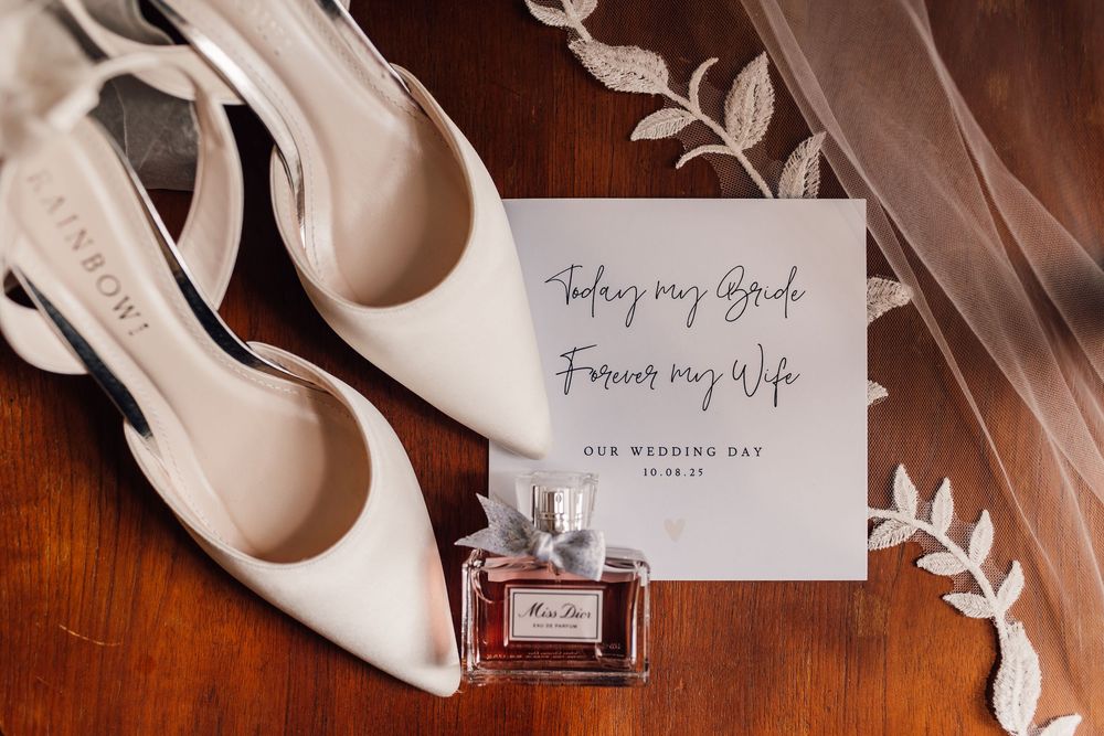 Elegant white bridal shoes and handwritten wedding day note cards arranged on wooden surface.