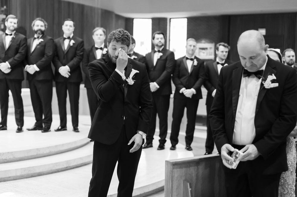 Emotional groom crying at the altar surrounded by groomsmen in black tuxedos.