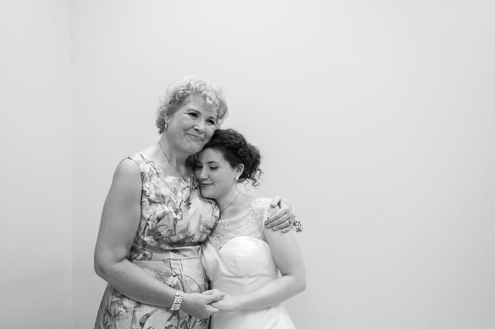A bride in a white gown shares a tender embrace with an older woman in a black and white portrait.