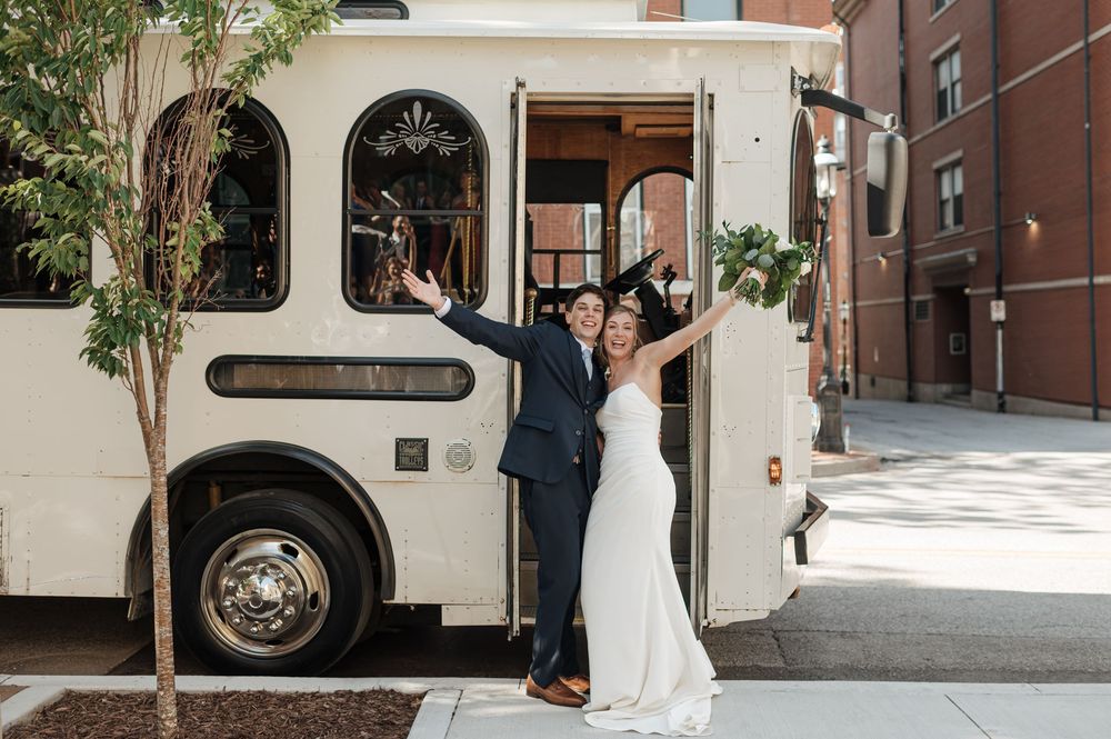 Happy bride and groom pose in front of white vintage trolley bus on their wedding day.