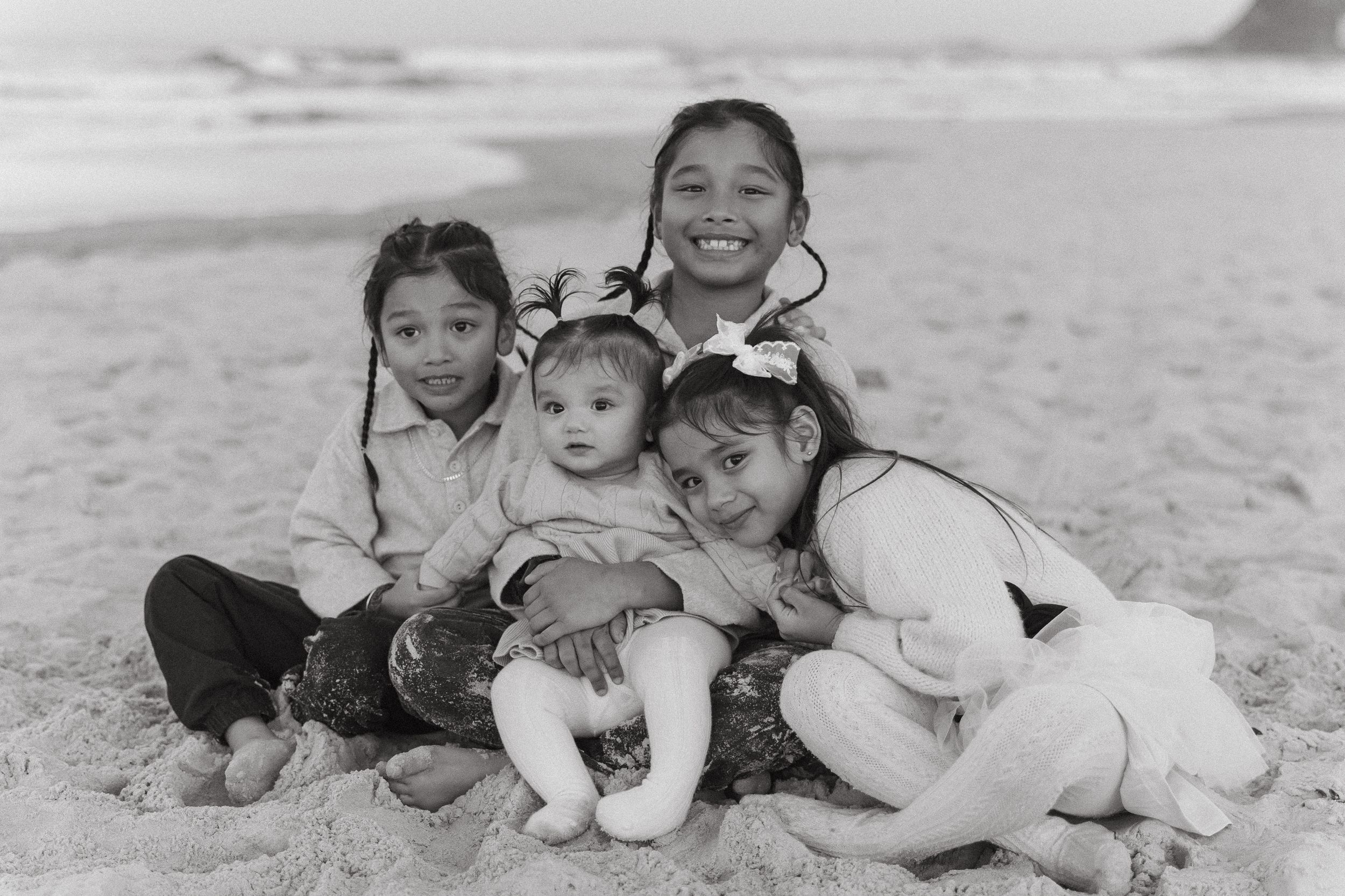 Family lying together on sandy beach during a black and white photo session.