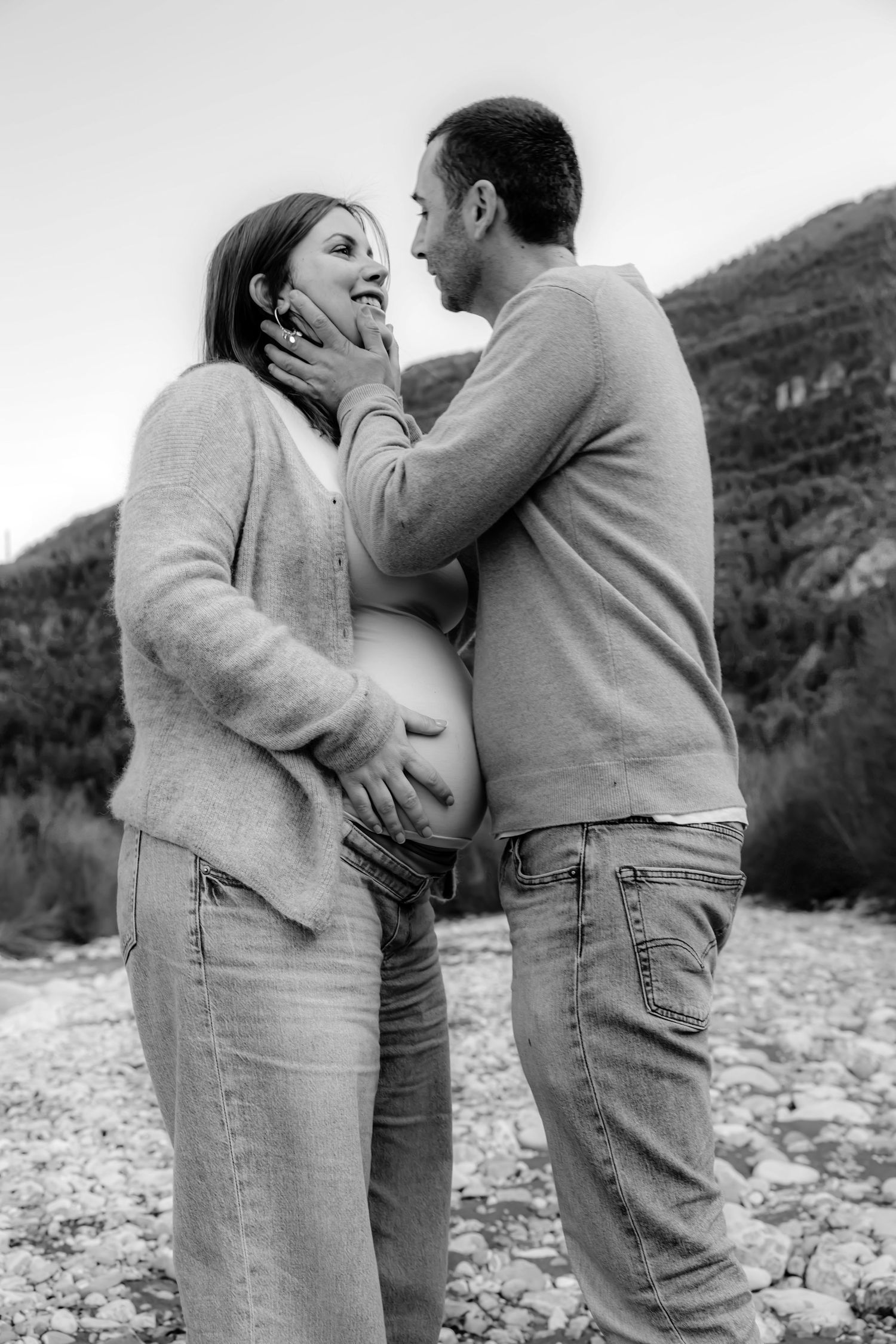 A romantic black and white sequence of a couple embracing outdoors by a rocky riverbed in casual attire.