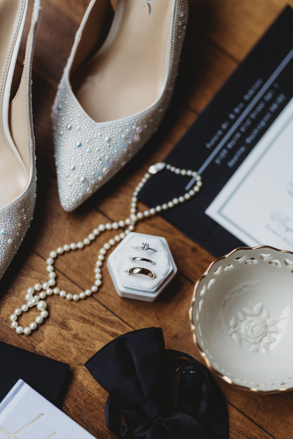 Wedding accessories including pearl necklace, white heels, and decorative items arranged on wooden surface.