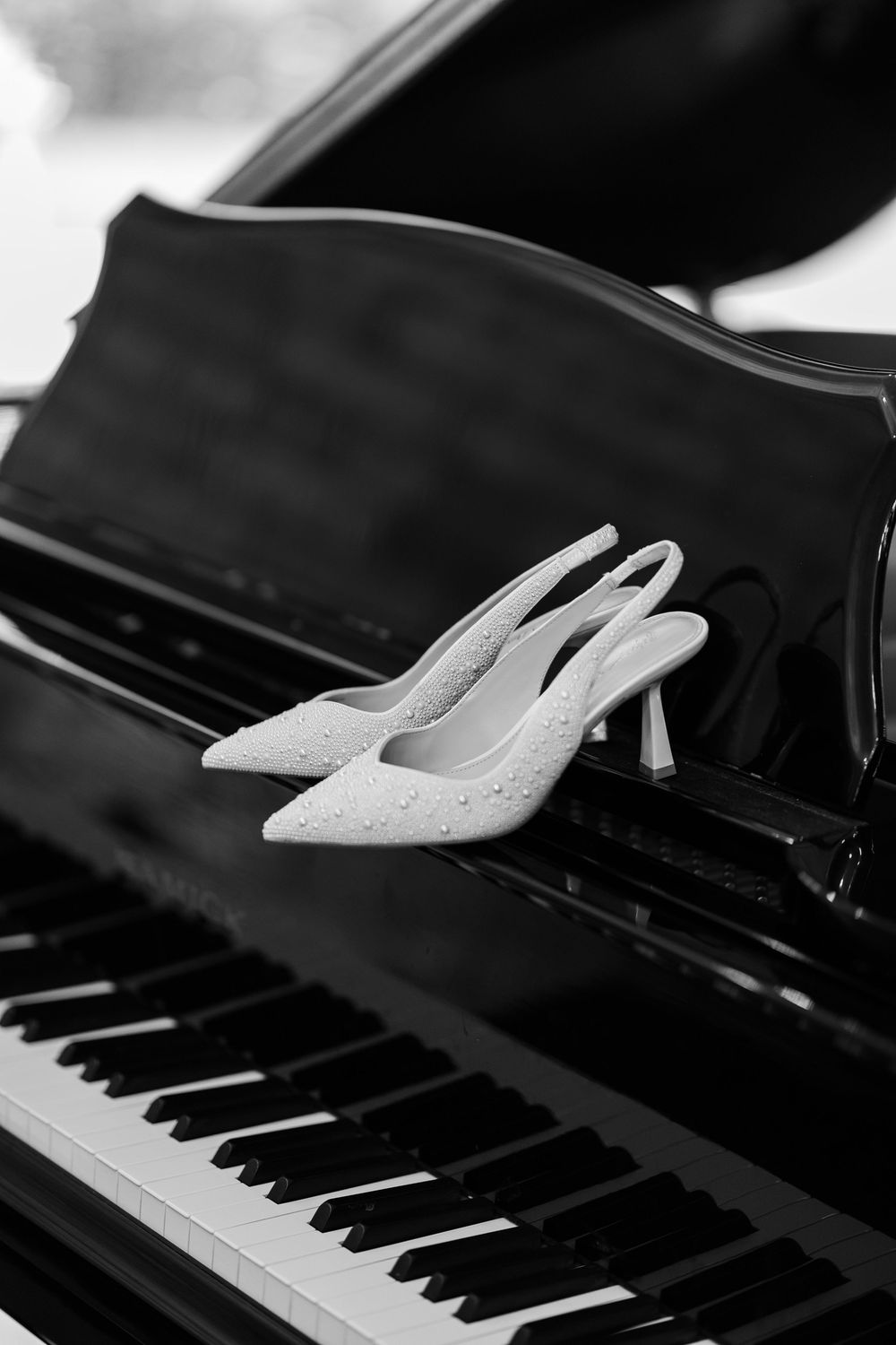 White bridal heels placed elegantly on black piano keys in dramatic lighting.