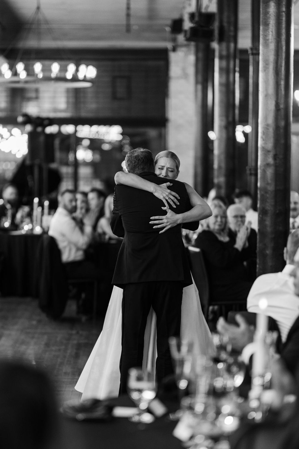 Black and white photo of wedding guests dancing in a dimly lit reception venue.