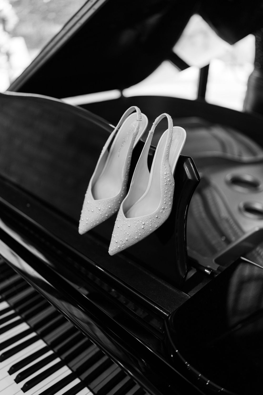 White bridal shoes placed on top of a black grand piano in dramatic lighting.