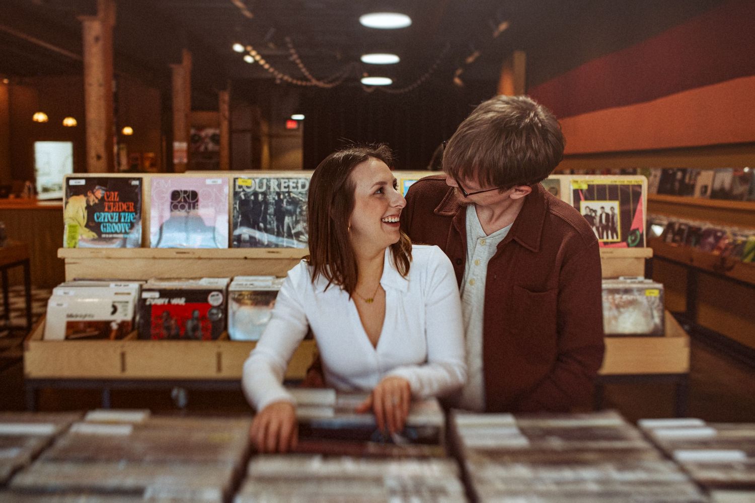 Two people lean in close while browsing through vinyl records at a music store. Indianapolis, Indiana engagement session.