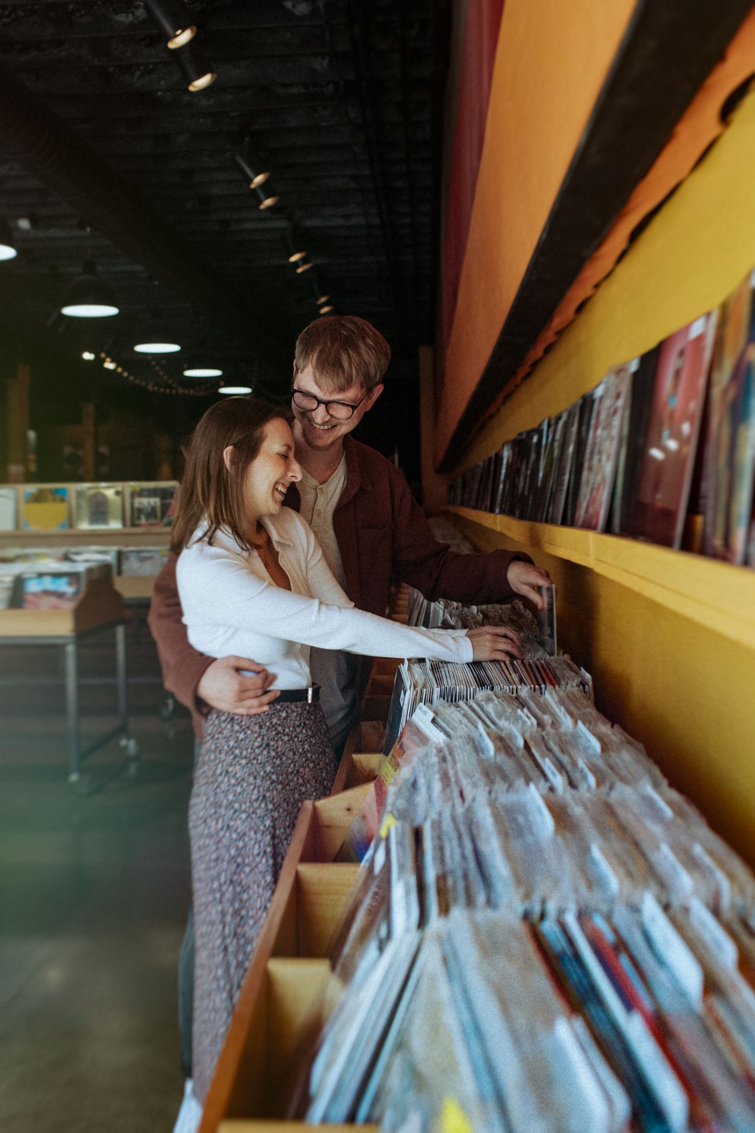 A person in a floral dress browses through vinyl records at a music store. Indianapolis, Indiana engagement session.