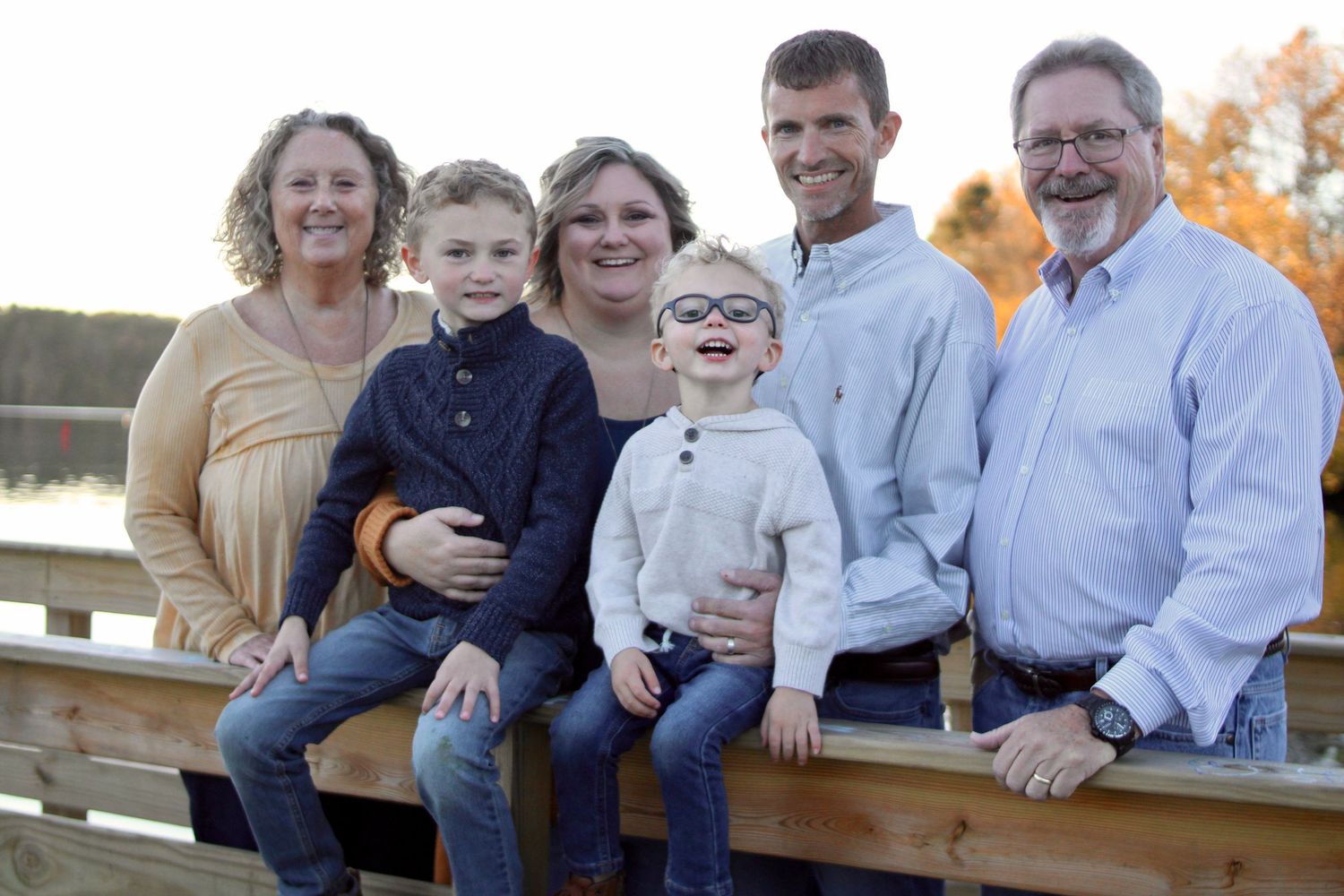 A family sits together on wooden benches outdoors during an autumn photoshoot in casual attire.