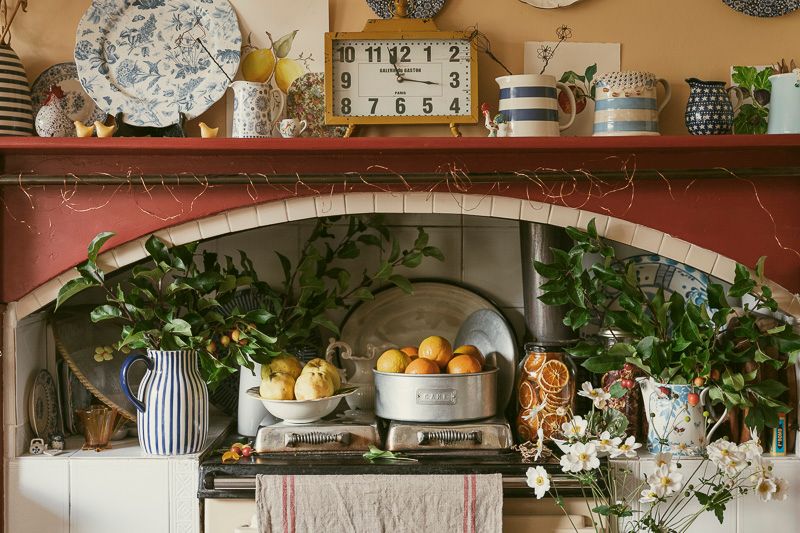 Editorial photo by Em Callaghan Photography, kitchen interior of Aga stove & mantle covered in fresh produce, foliage and vintage crockery.