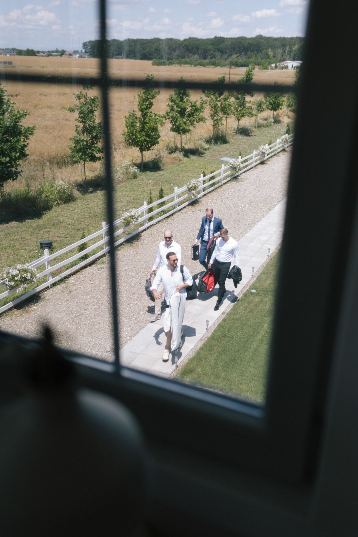 View through window of guests walking along white gravel path at outdoor venue.