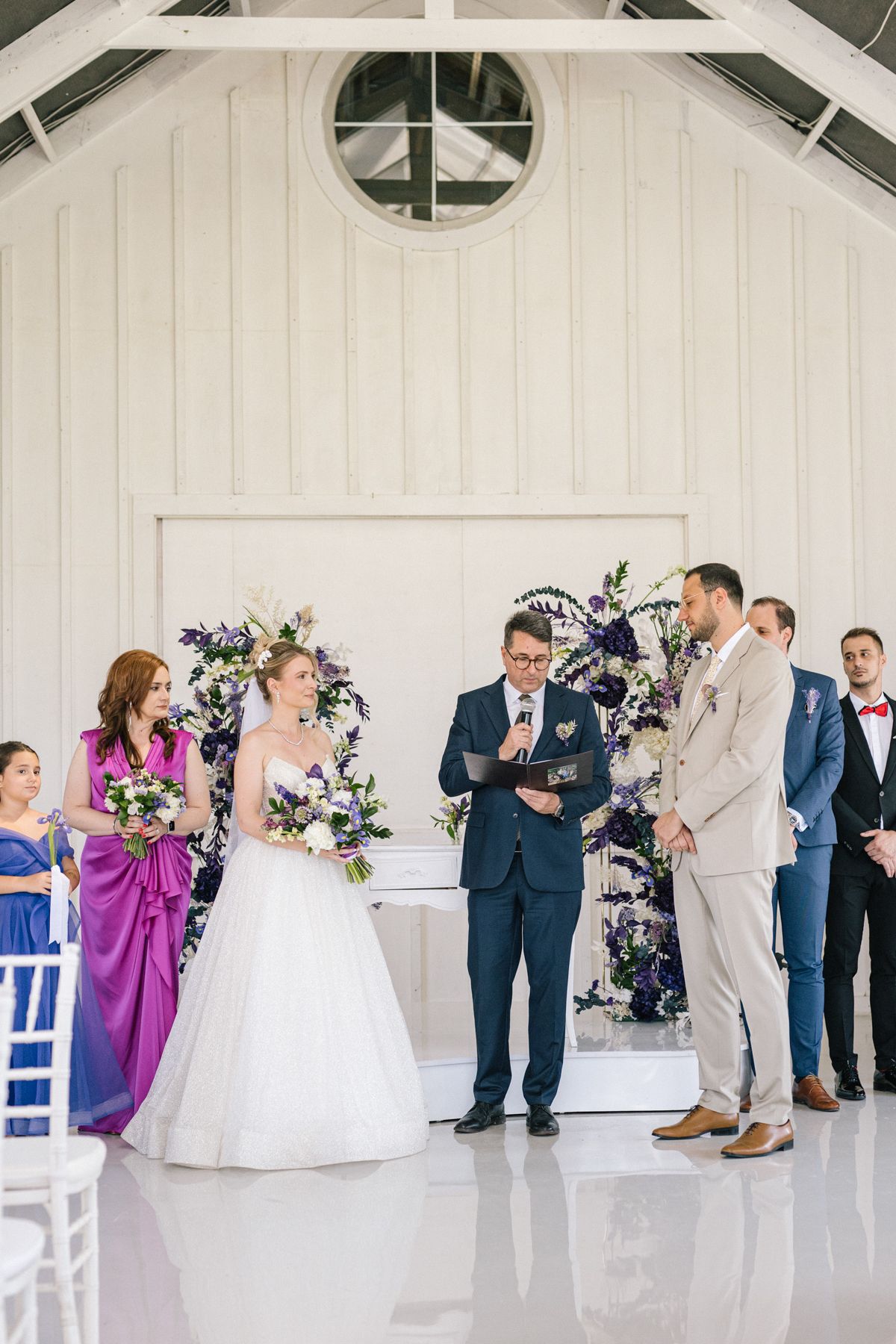 Wedding ceremony in progress inside a white chapel with floral decorations.