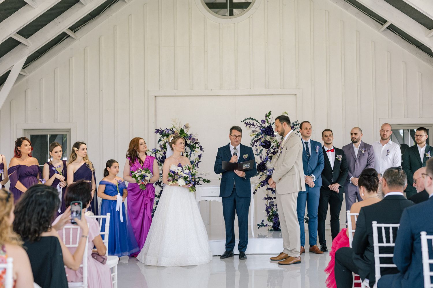 Wide view of wedding ceremony inside modern white chapel with guests in attendance.