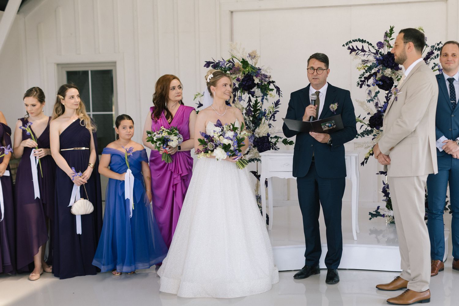 Wedding party in purple and blue attire gathered during indoor ceremony.