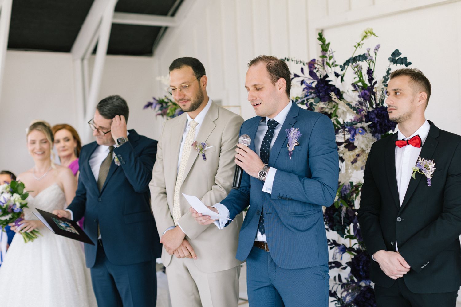 Groomsmen in various colored suits stand together during wedding ceremony.