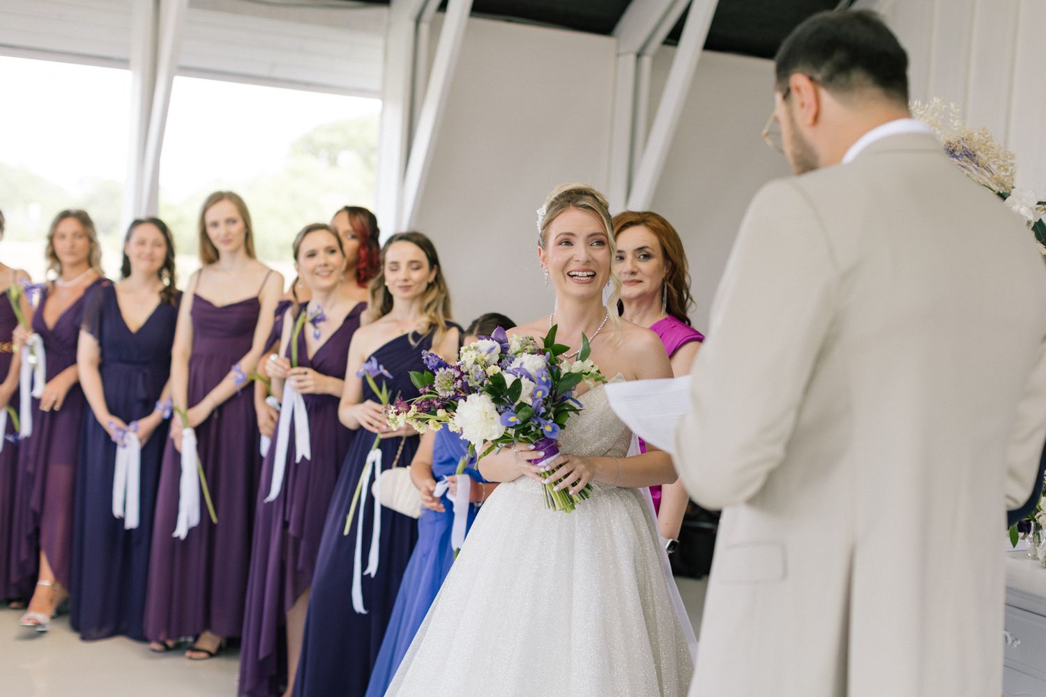 Wedding party members gather in a modern white venue with elegant formal attire.