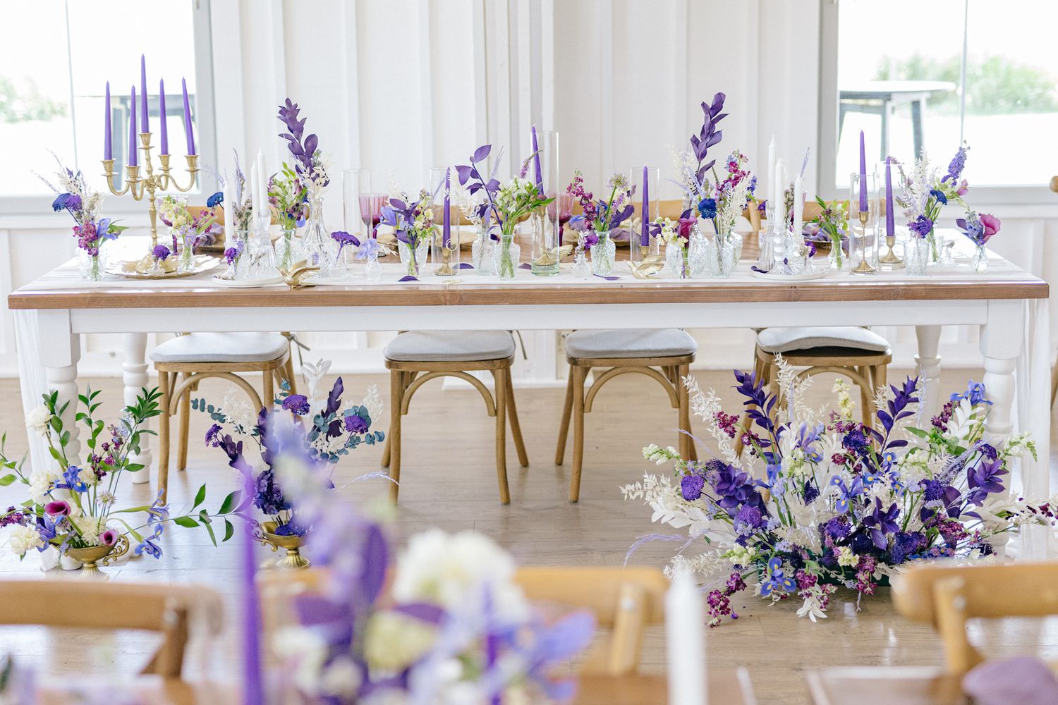 Purple floral centerpieces with delicate blooms and candles line a wedding reception table setting.