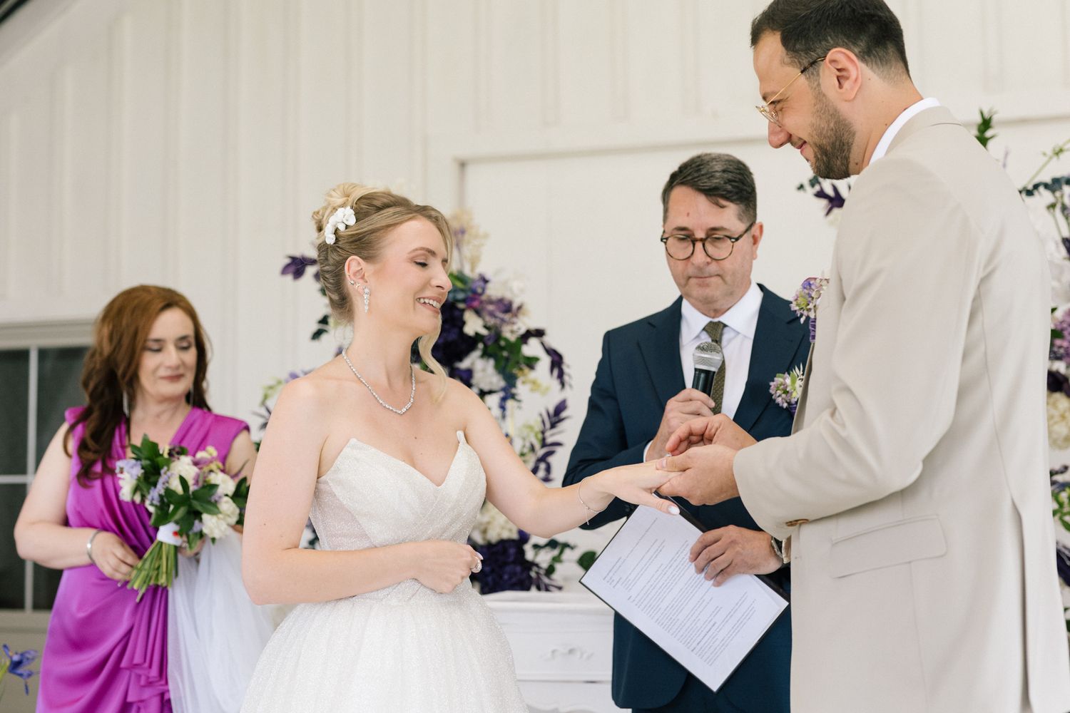 Wedding ceremony moments captured in a bright white venue with floral decorations.