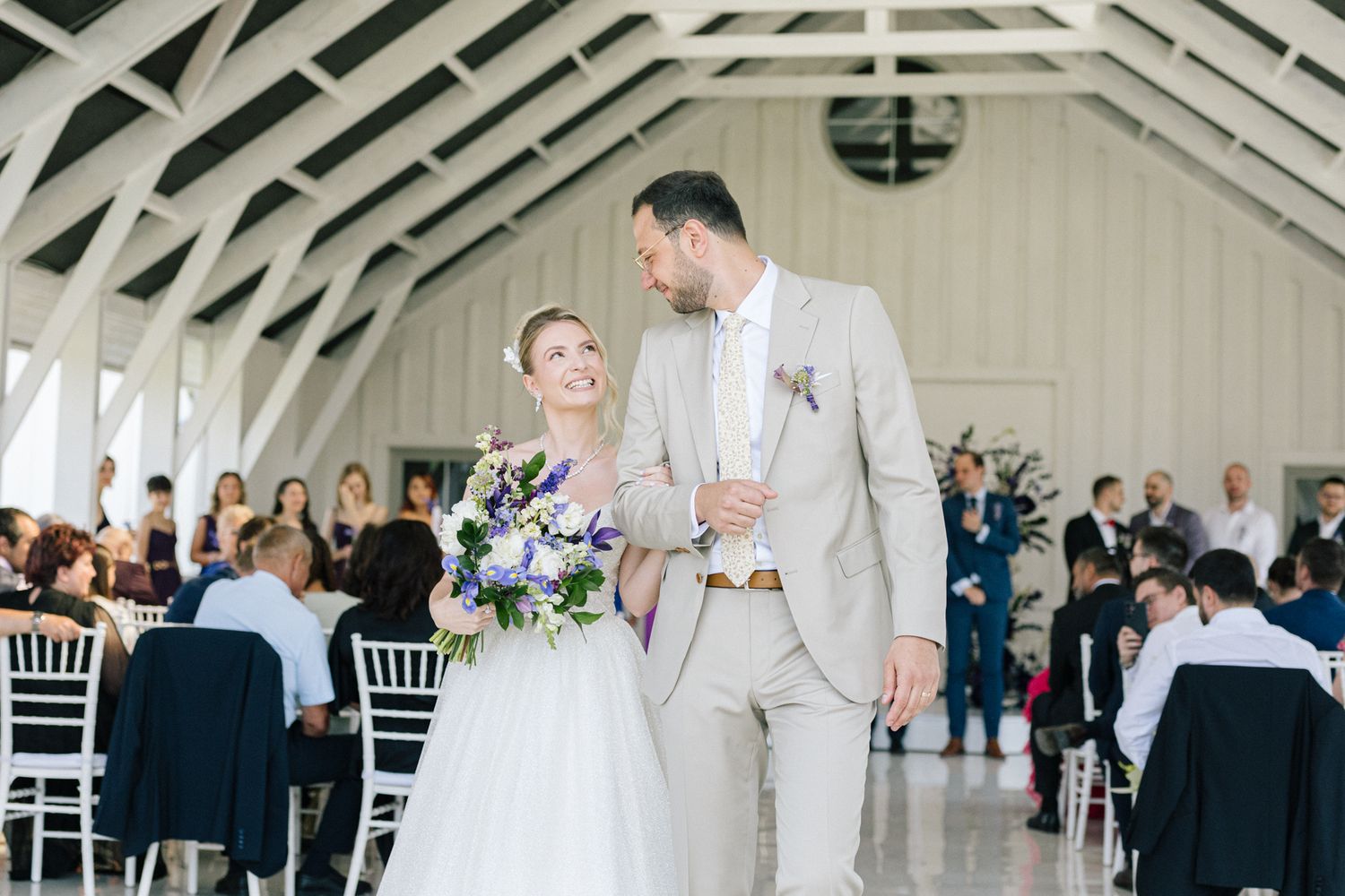 Couple shares a dance moment in a bright indoor venue with white chairs and cathedral ceiling.