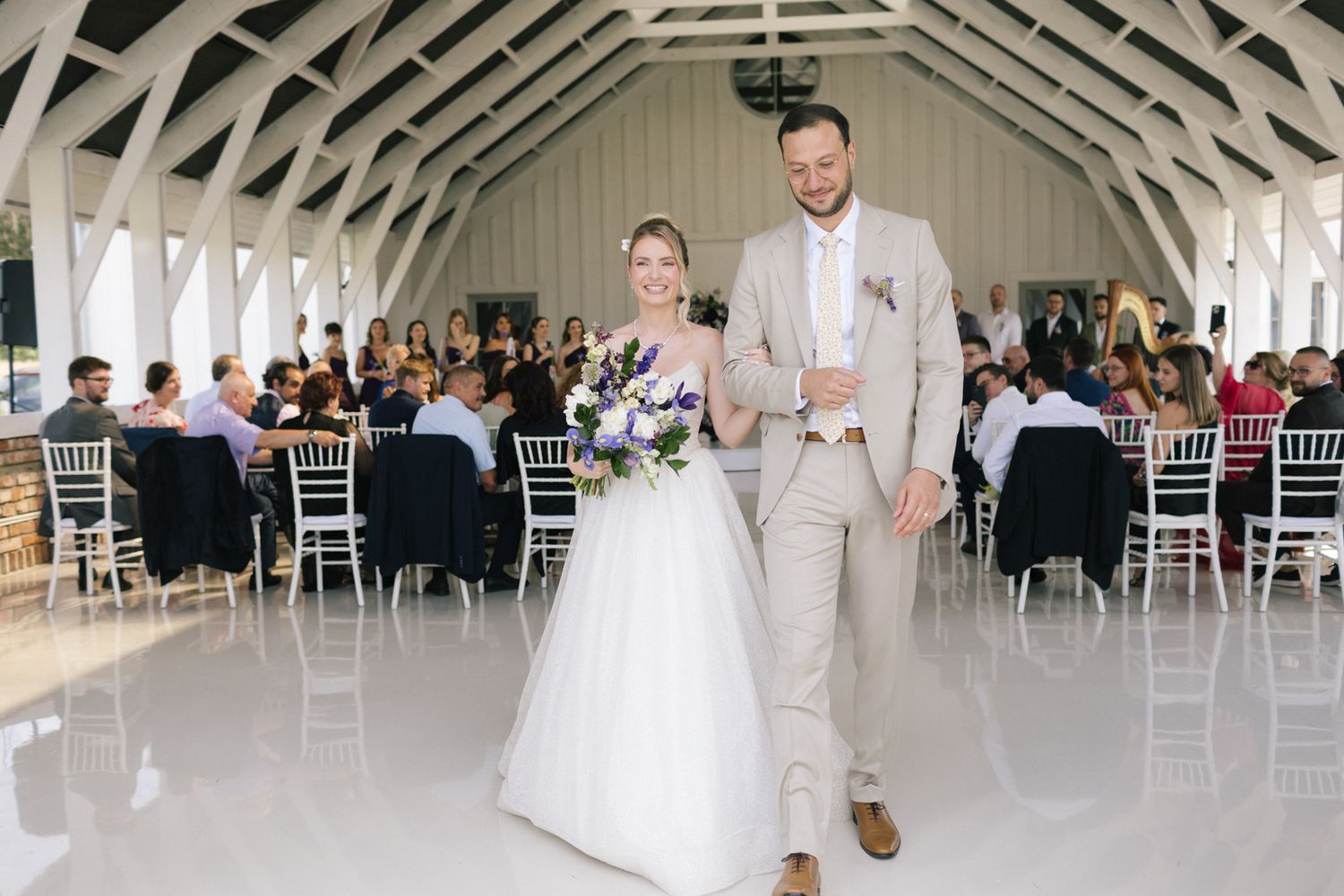 Wedding celebration in a bright indoor venue with exposed beams and white chairs.