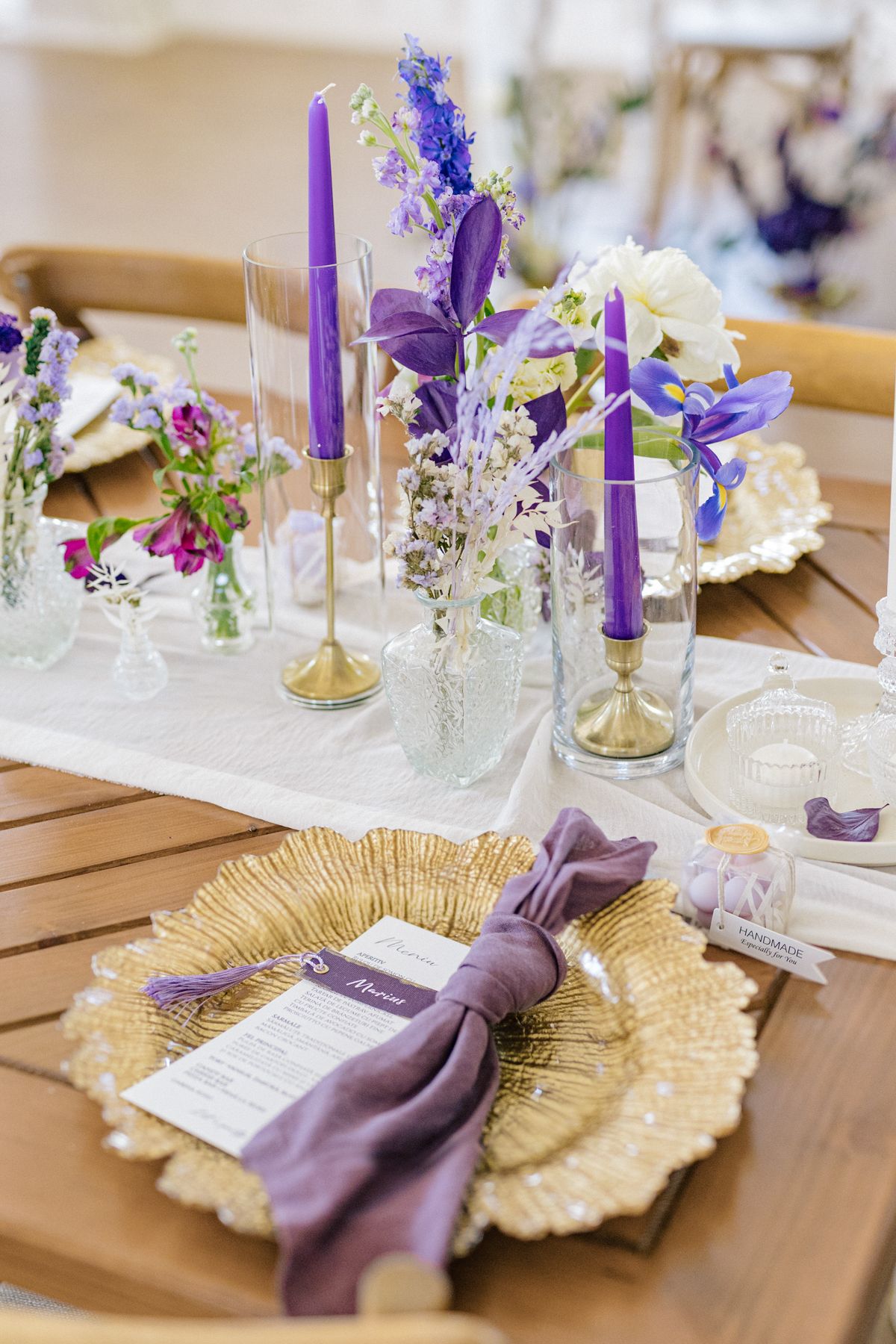 Gold charger plates with purple napkins and floral accents create an elegant place setting.