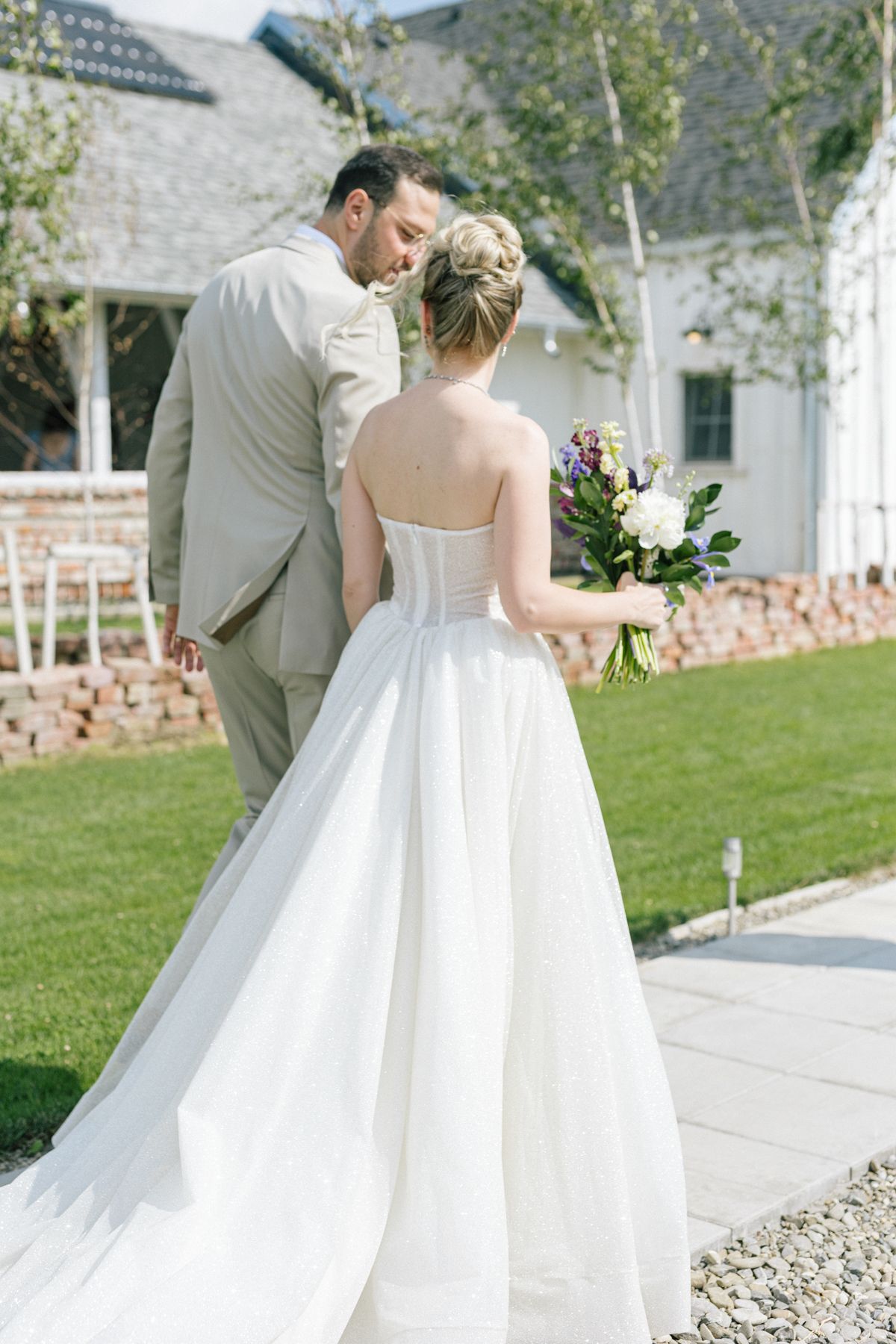 Wedding couple walks along a stone path outside a white building on a sunny day.