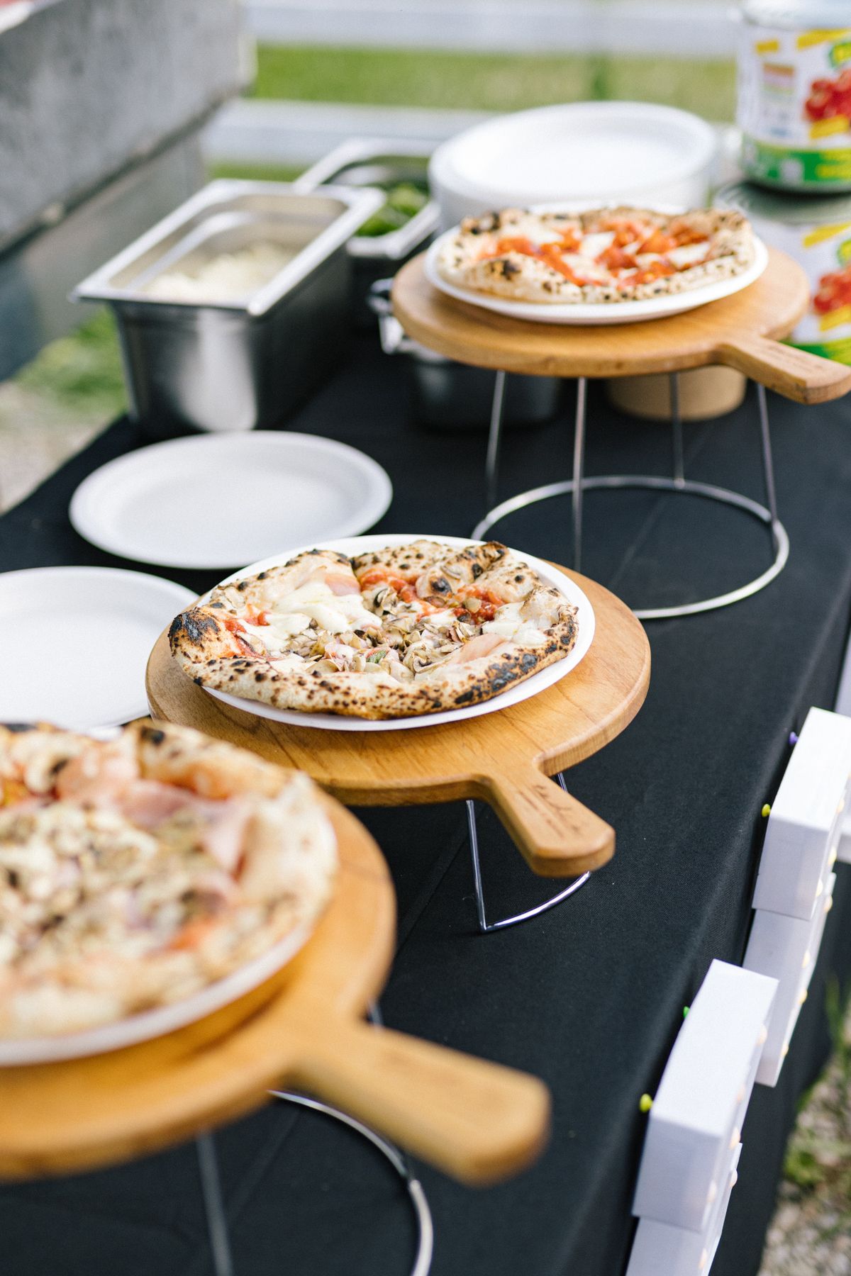 Wooden pizza boards display various pizzas on a black tablecloth at a casual wedding reception.