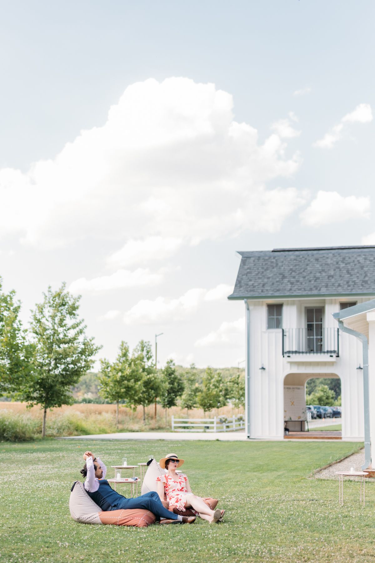White modern farmhouse wedding venue sits on a green lawn under blue skies.