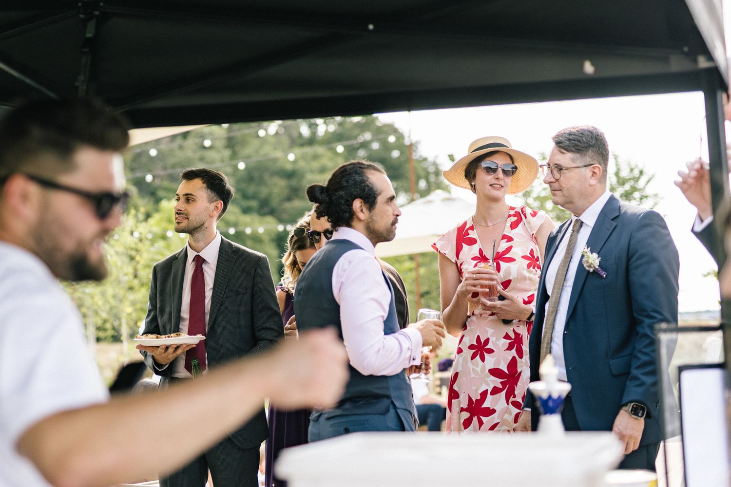 Guests mingle under covered outdoor area during wedding celebration.