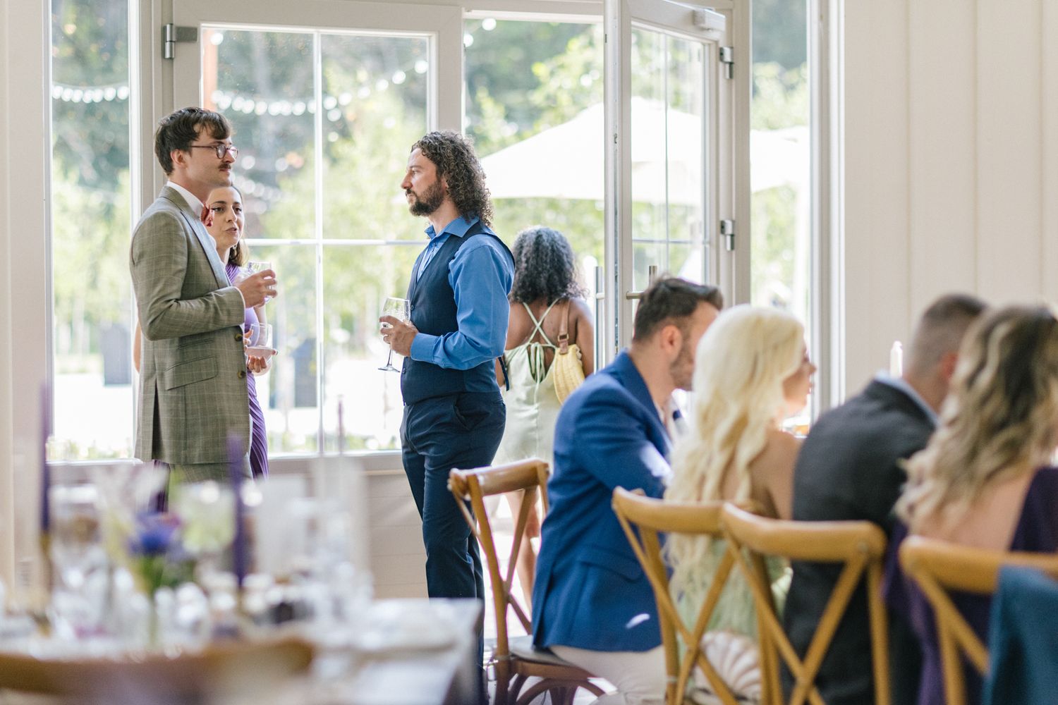Wedding guests seated in bright indoor venue with large windows.