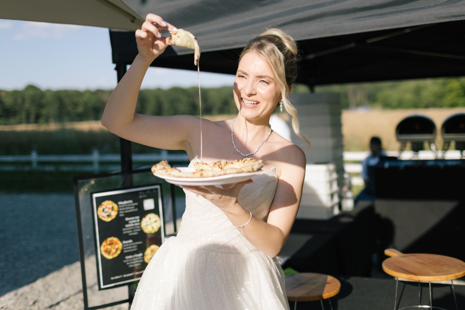 Woman in wedding dress reaches for food at an outdoor event.