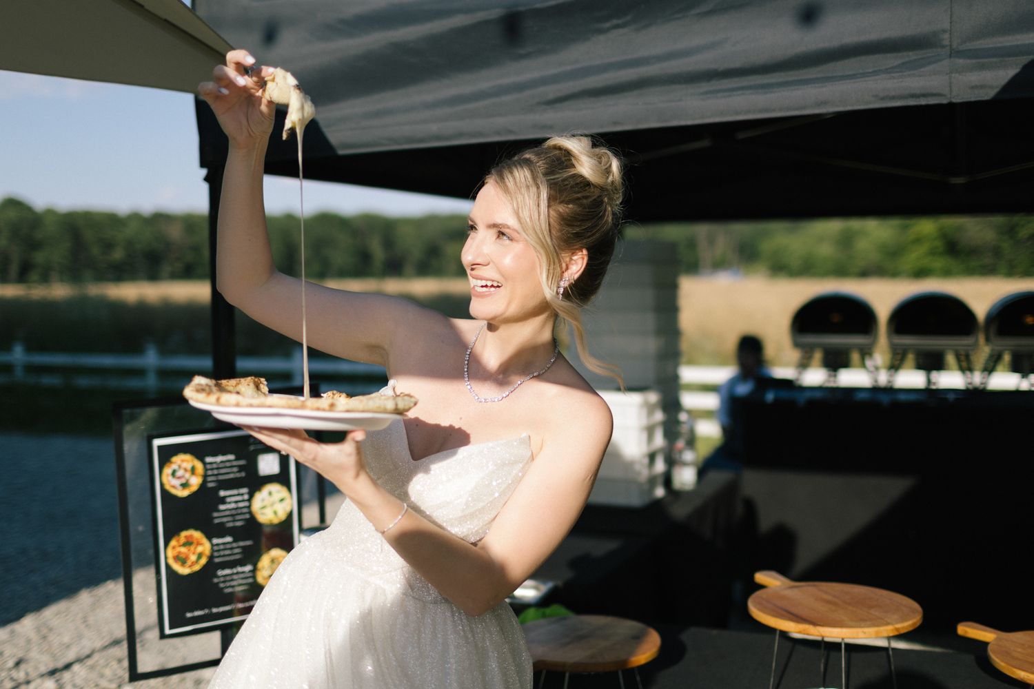Woman in white wedding dress reaches up to grab food from a vendor.