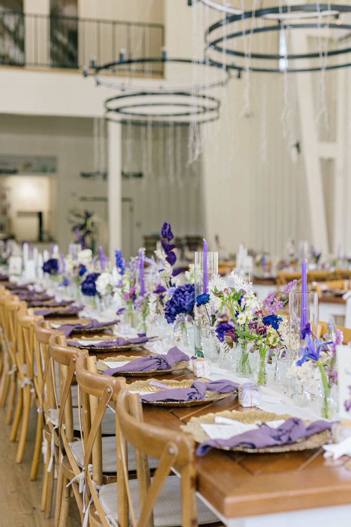 Elegant reception hall setup with wooden chairs and purple floral table decorations.