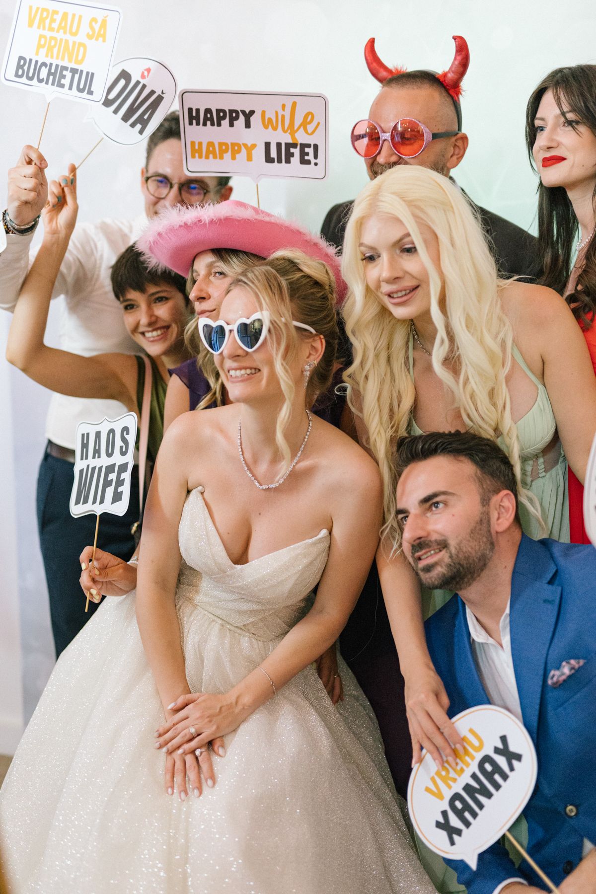 Wedding party poses with fun photo props and signs during a lively celebration.