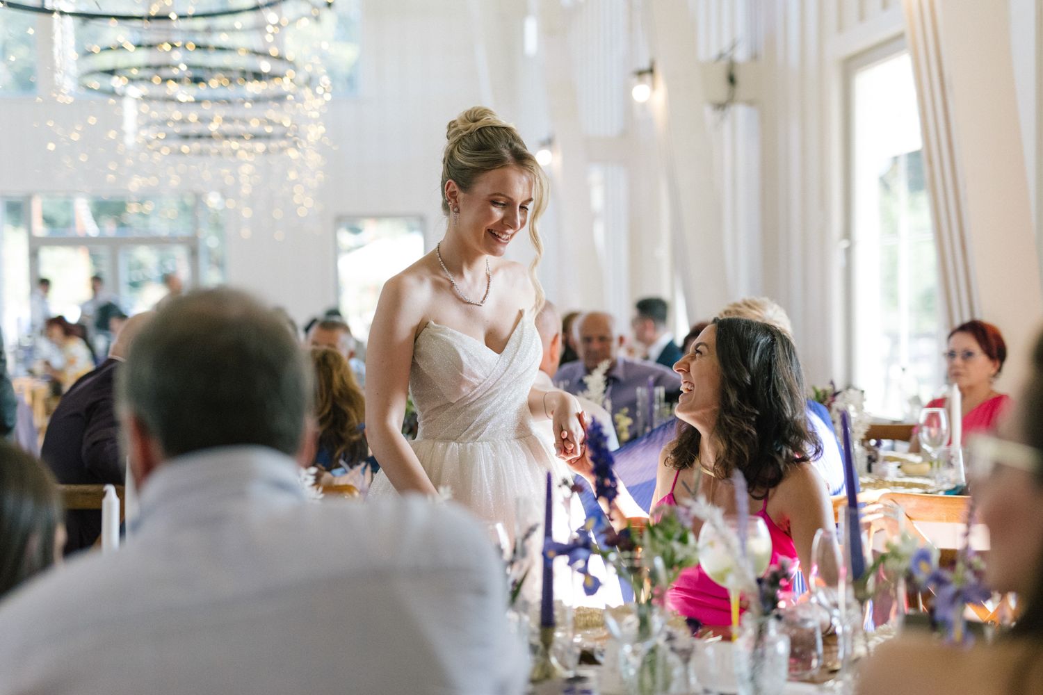 Wedding guests mingle and celebrate at an elegant reception with crystal chandeliers overhead.