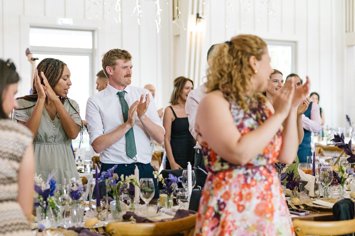 Wedding guests applaud and celebrate during an indoor reception.